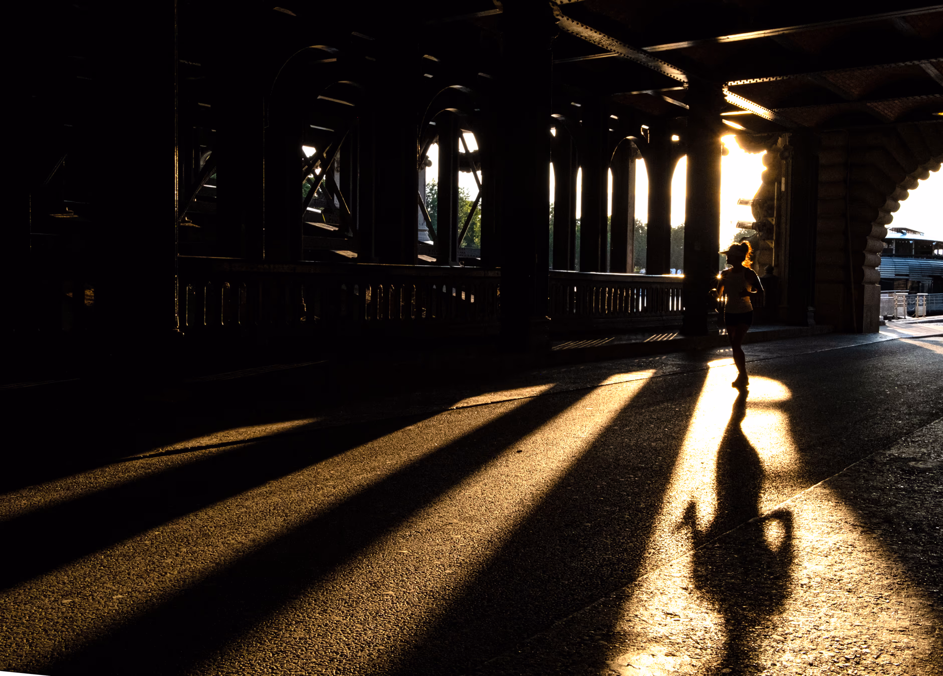 Persona bajo un puente del Sena en contraluz dramático con sombras largas en el suelo — street photography Fujifilm X-E4