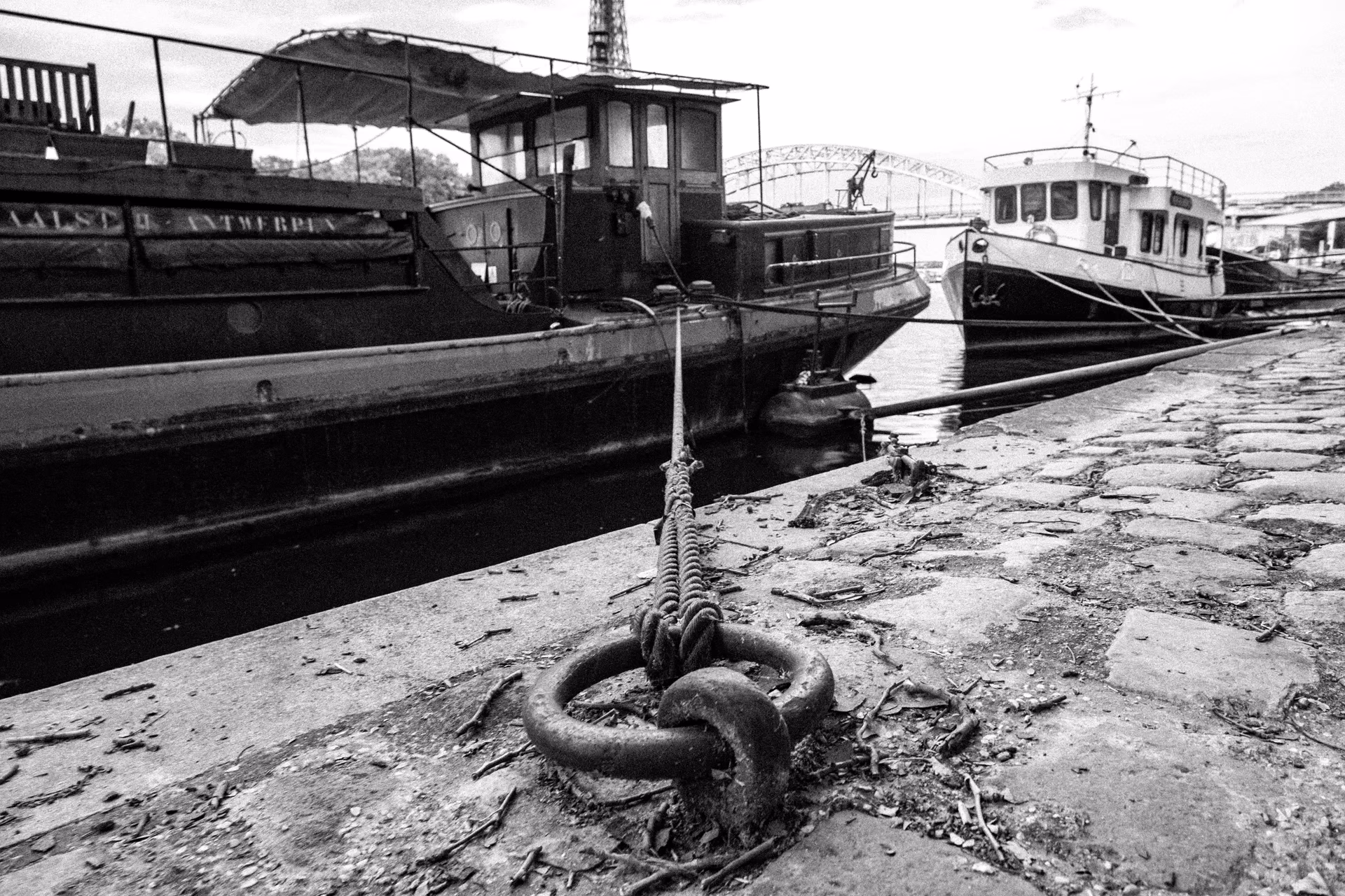 Foto en blanco y negro de embarcaciones fluviales en un muelle del Sena con argolla de amarre en primer plano — Fujifilm X-E4