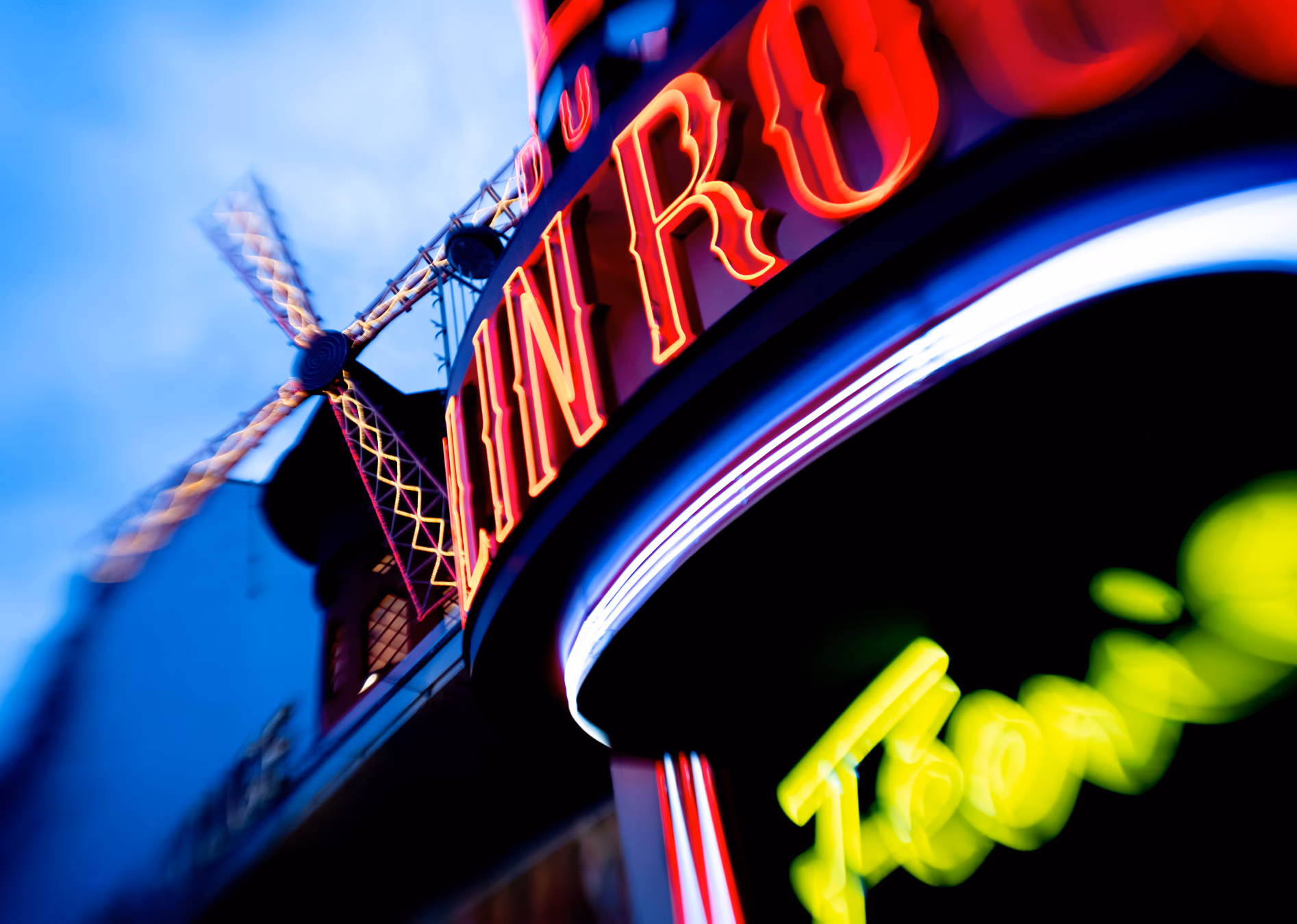 Letrero de neón brillante en rojo y amarillo en una fachada parisina con cielo azul — Fujifilm X-E4 con Lensbaby Sweet 22
