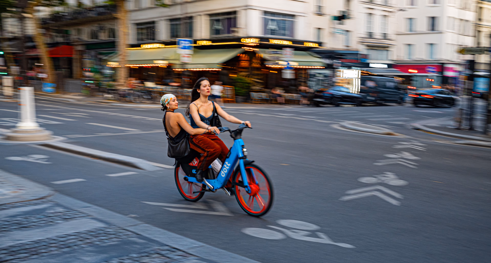 Dos mujeres en bicicletas de préstamo roja y azul recorren una calle animada de París — street photography Nikon Zfc
