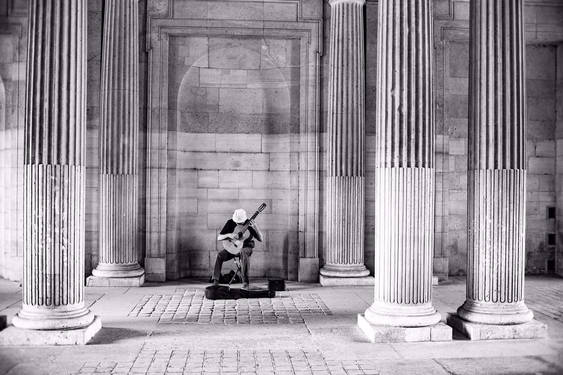 Músico callejero con guitarra sentado entre columnas clásicas en París — street photography Nikon Zfc