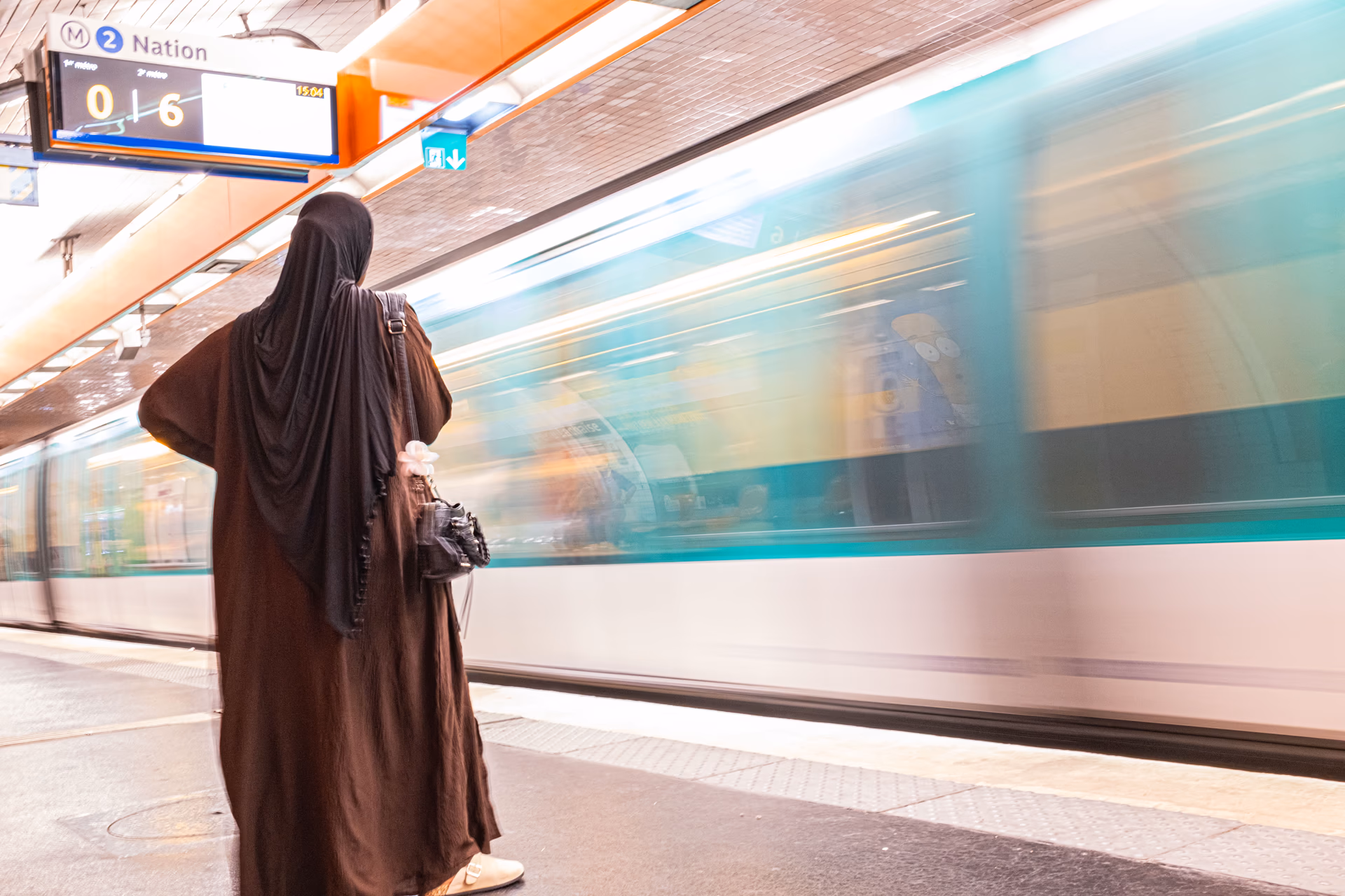 Mujer con abrigo café espera en la estación de metro Nation en París, tren pasando con desenfoque de movimiento