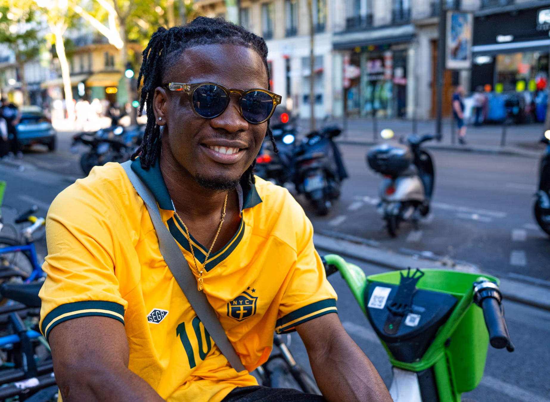 Hombre sonriente con camisa amarilla y lentes de sol en una calle animada de París con motos — street photography Fujifilm X100V