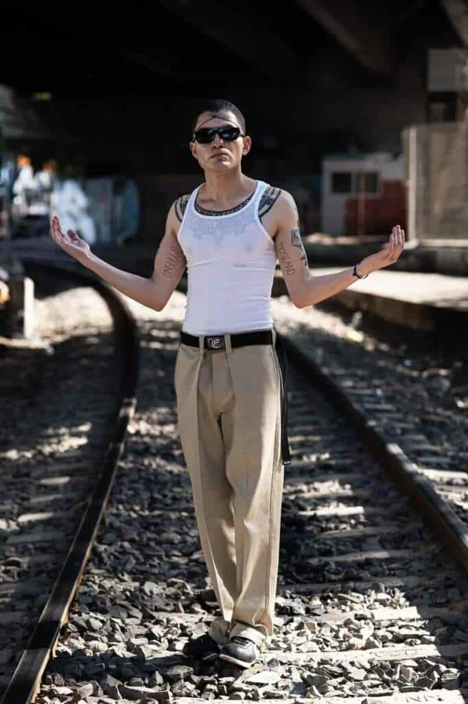 Hombre con tatuajes y gafas de sol sobre vías de tren, evocando el filtro México en el cine.