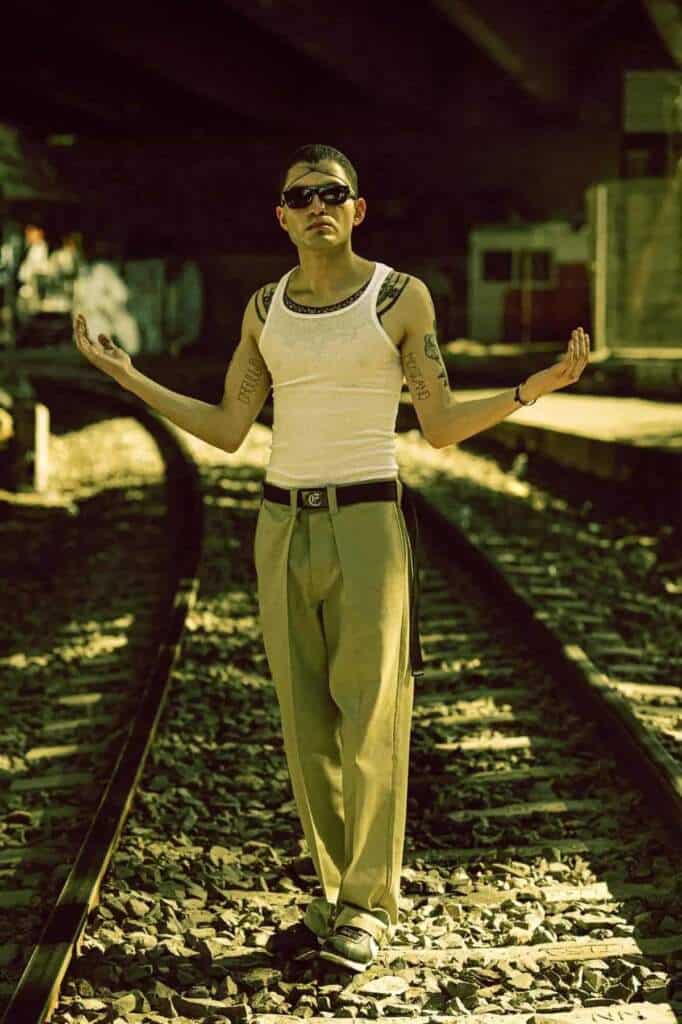 Hombre con tatuajes y gafas de sol en vías de tren, con el filtro México en el cine.