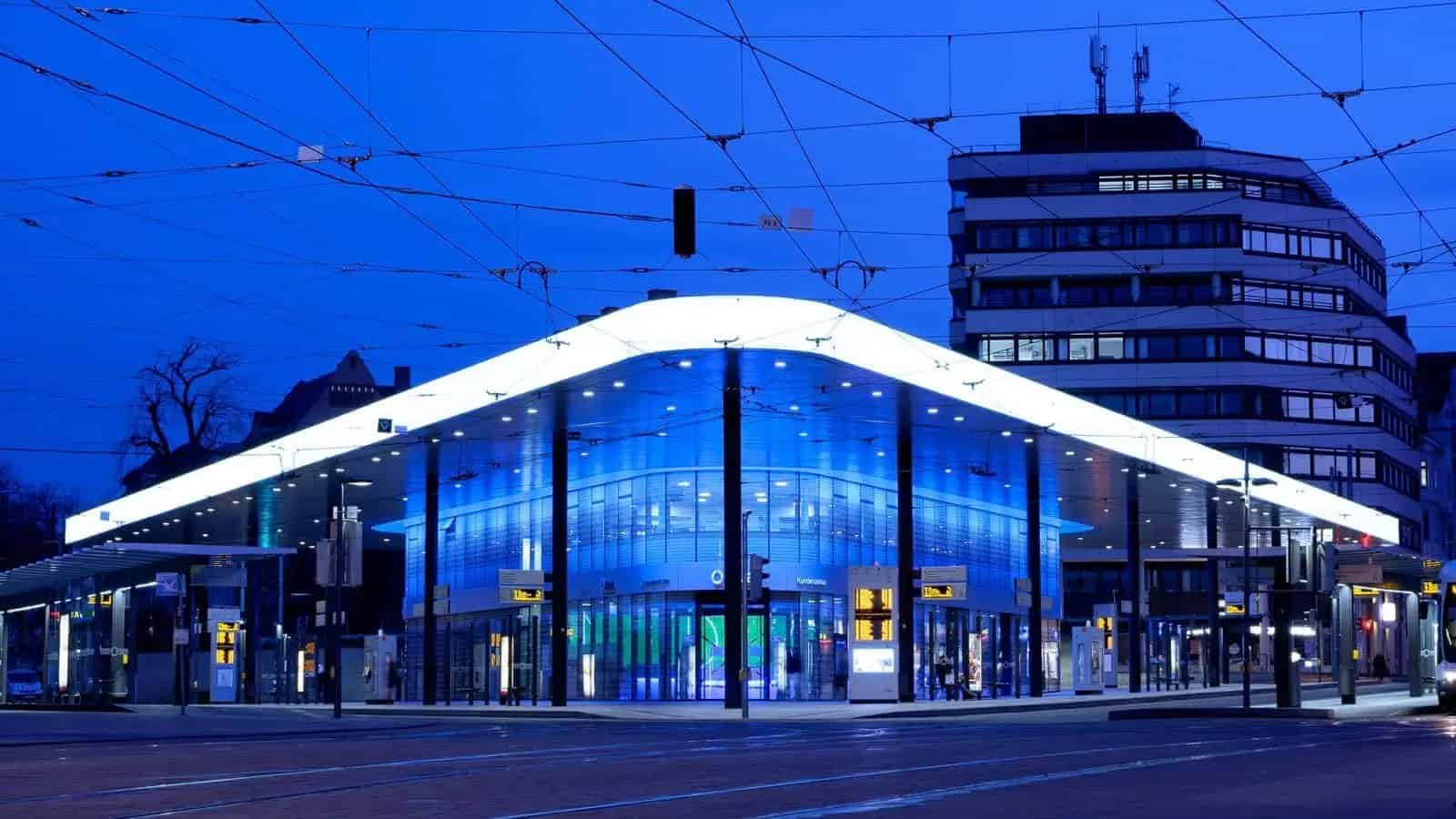 Edificio moderno con iluminación azul y blanca, con cables eléctricos cruzando el cielo.