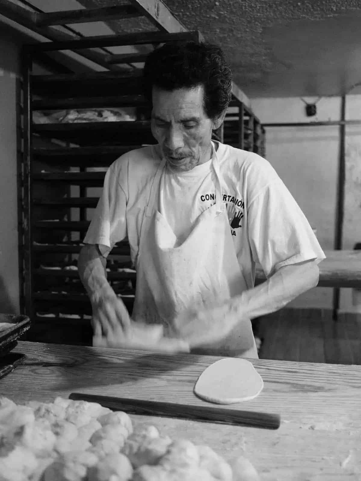 Panadero mexicano amasa masa en panadería artesanal con poca luz.