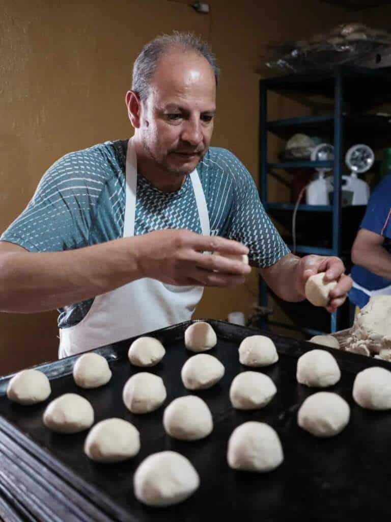 Panadero formando bolitas de masa para pan en una panadería mexicana.