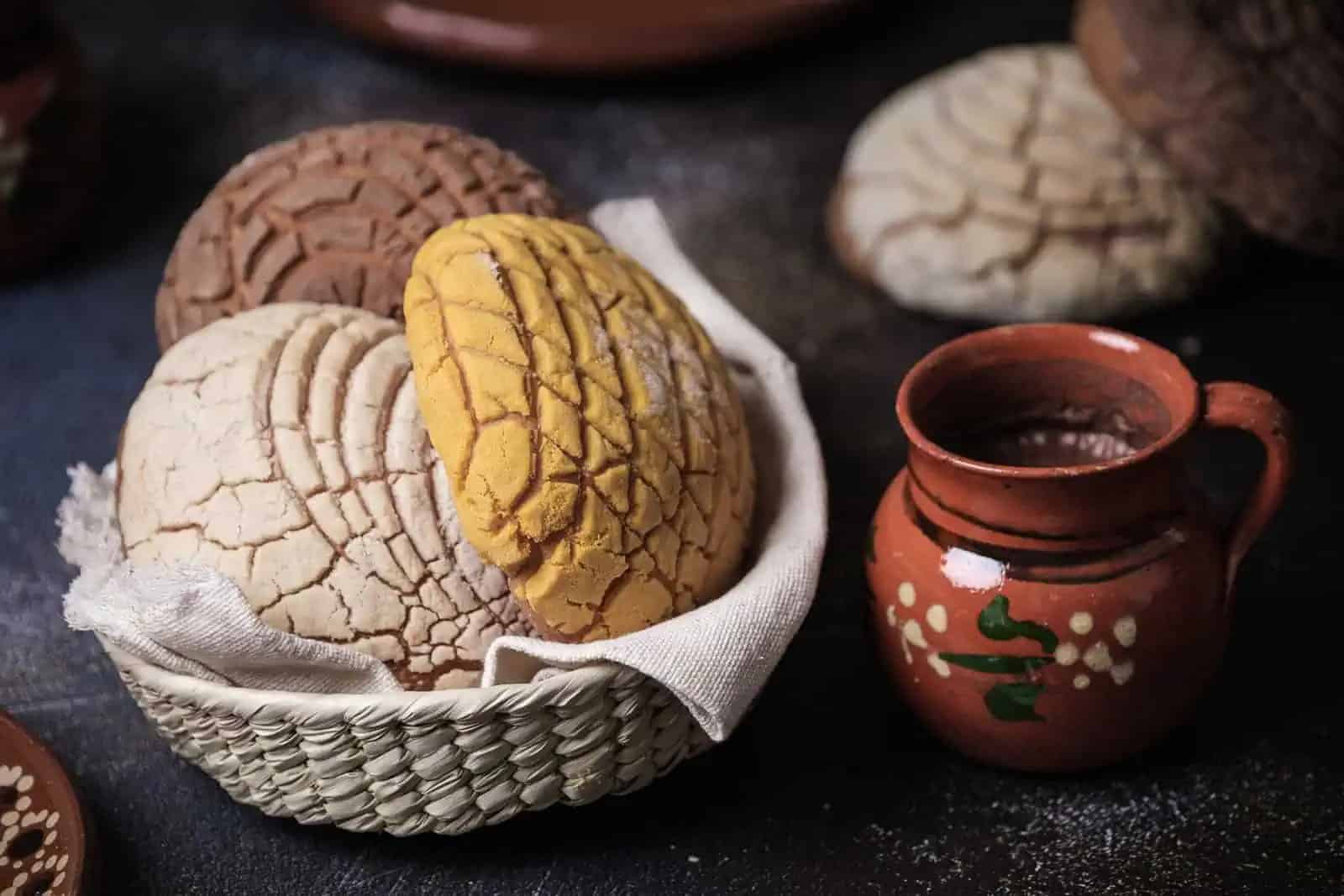 Canasta de conchas de pan dulce mexicano y taza de chocolate artesanal.