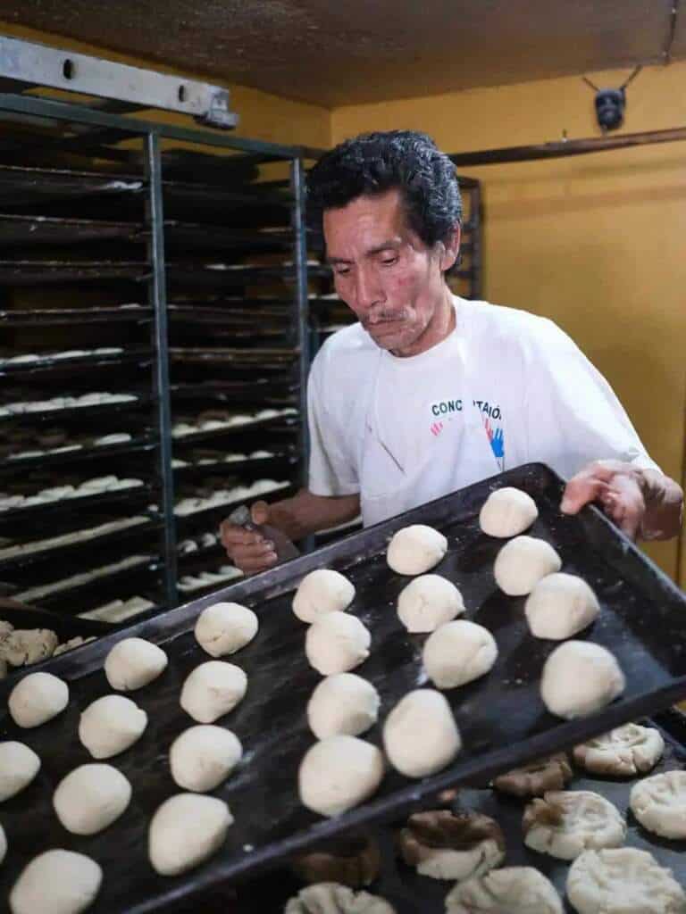 Panadero mexicano acomoda masa en charola, fotografía de reportaje en panadería mexicana.
