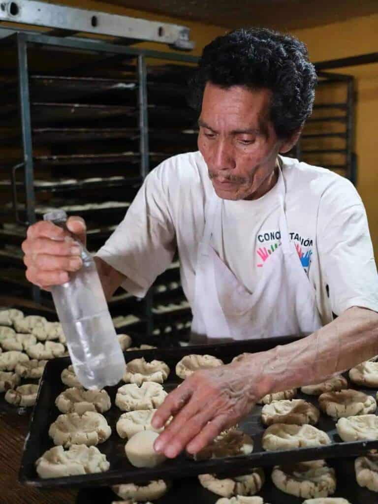 Panadero mexicano rocía agua a pan dulce en panadería artesanal de Metepec.