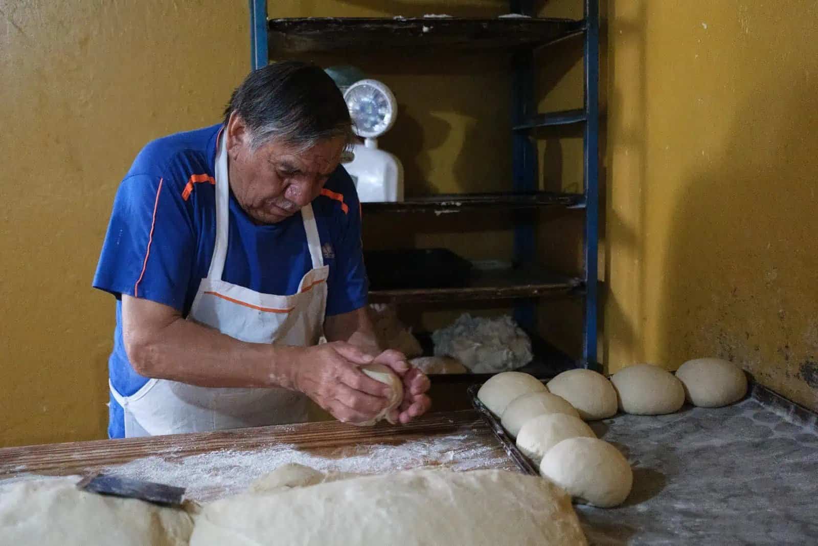 Panadero mexicano da forma a masa de pan en panadería artesanal.