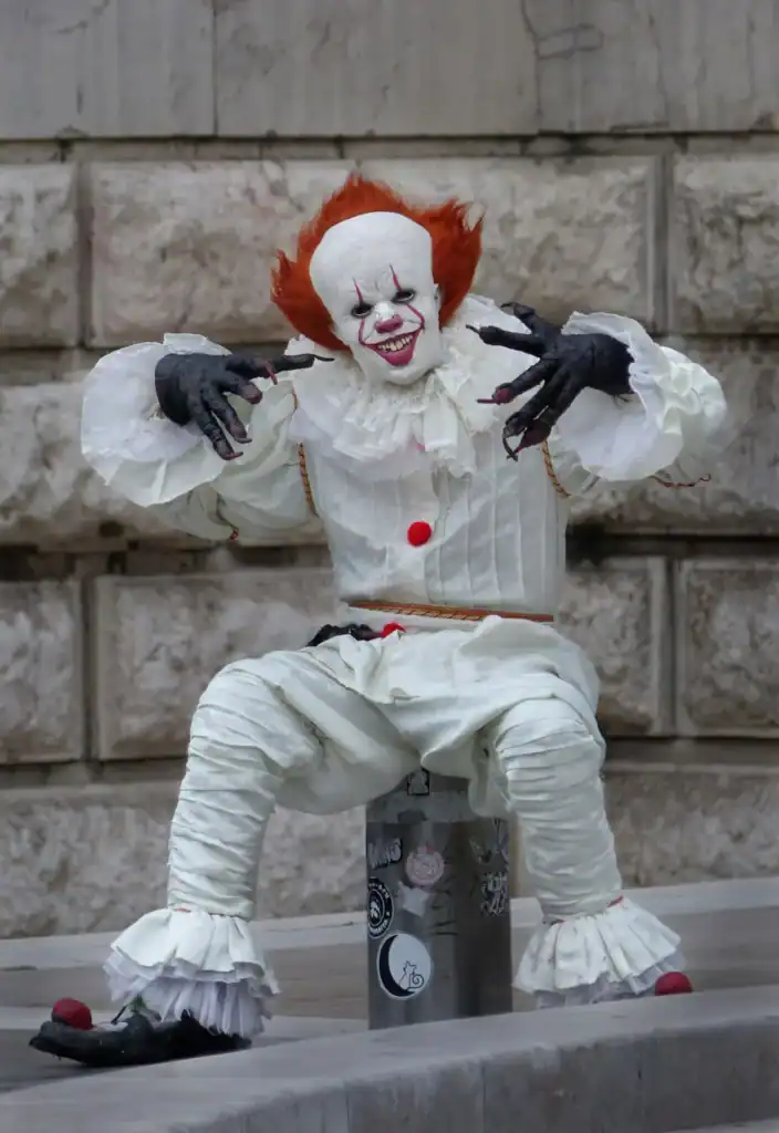 Un payaso espeluznante, con el pelo rojo y un traje blanco, está sentado sobre una columna.