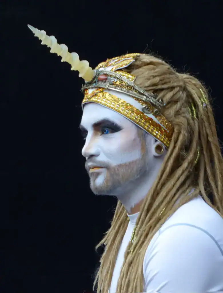 Hombre con la cara blanca, un ojo azul y un tocado con forma de unicornio