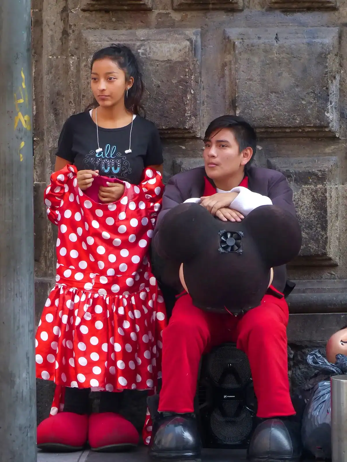 Una joven pareja vestida con trajes de época espera a los clientes frente a una pared de piedra.