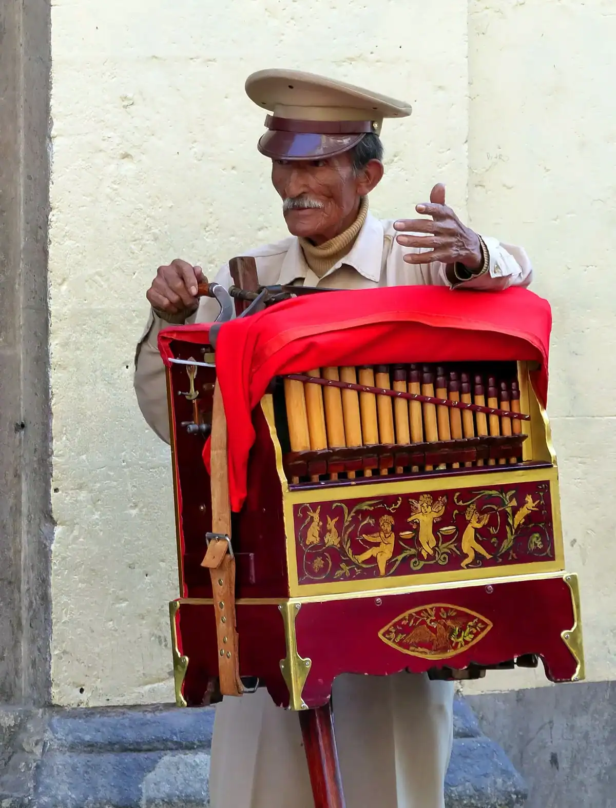 Un hombre mayor con bigote toca un organillo cubierto con un paño rojo
