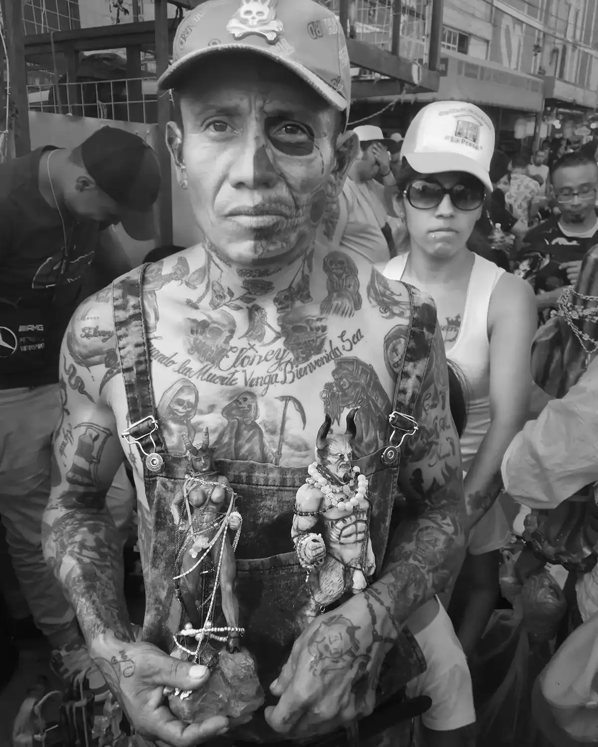 Un hombre con la cara pintada y tatuajes sostiene unas figuras en las manos