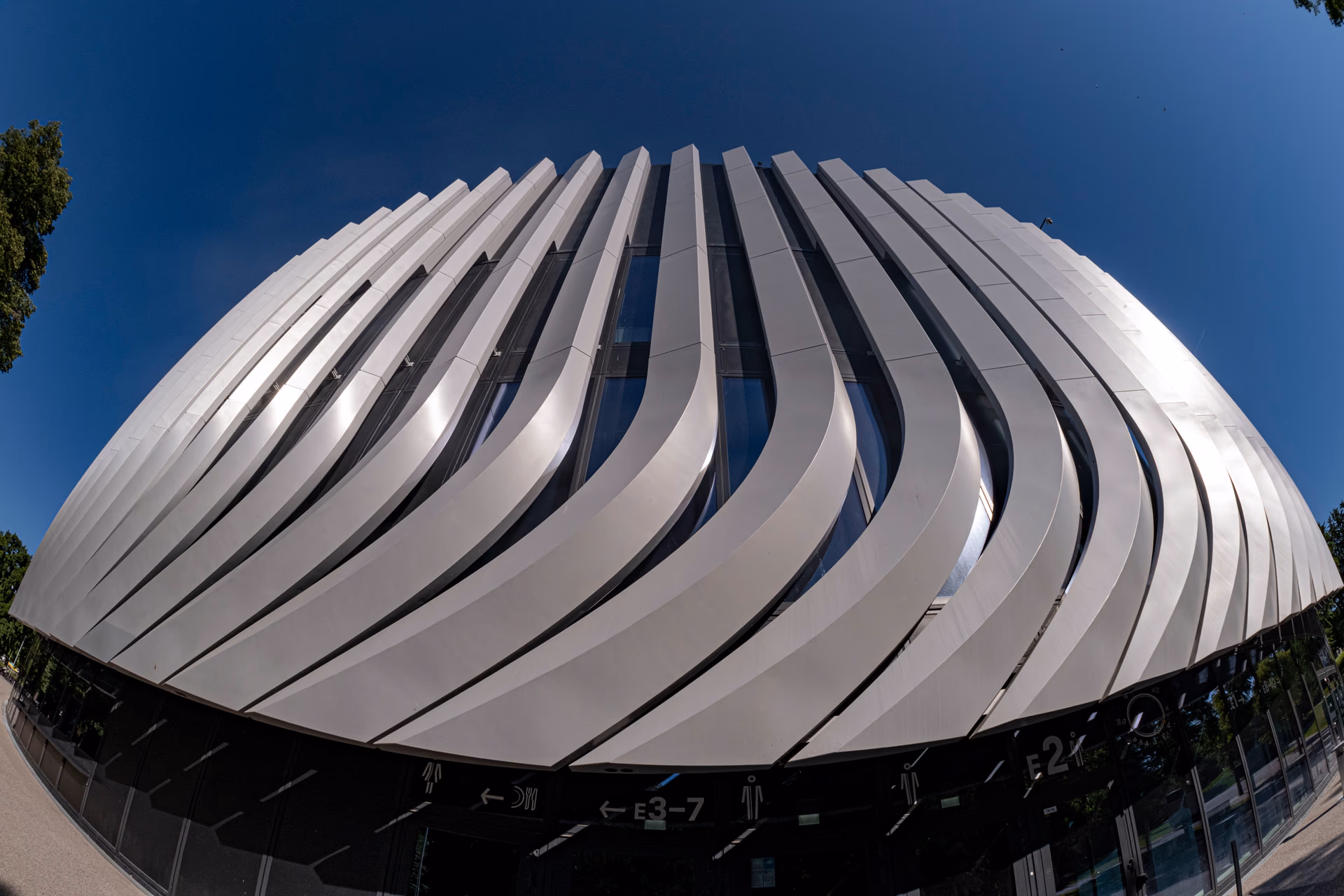 Arquitectura moderna con fachada ondulada y cielo azul, capturada con el Laowa 4,5-10 mm f/2.8 Fisheye Zoom.