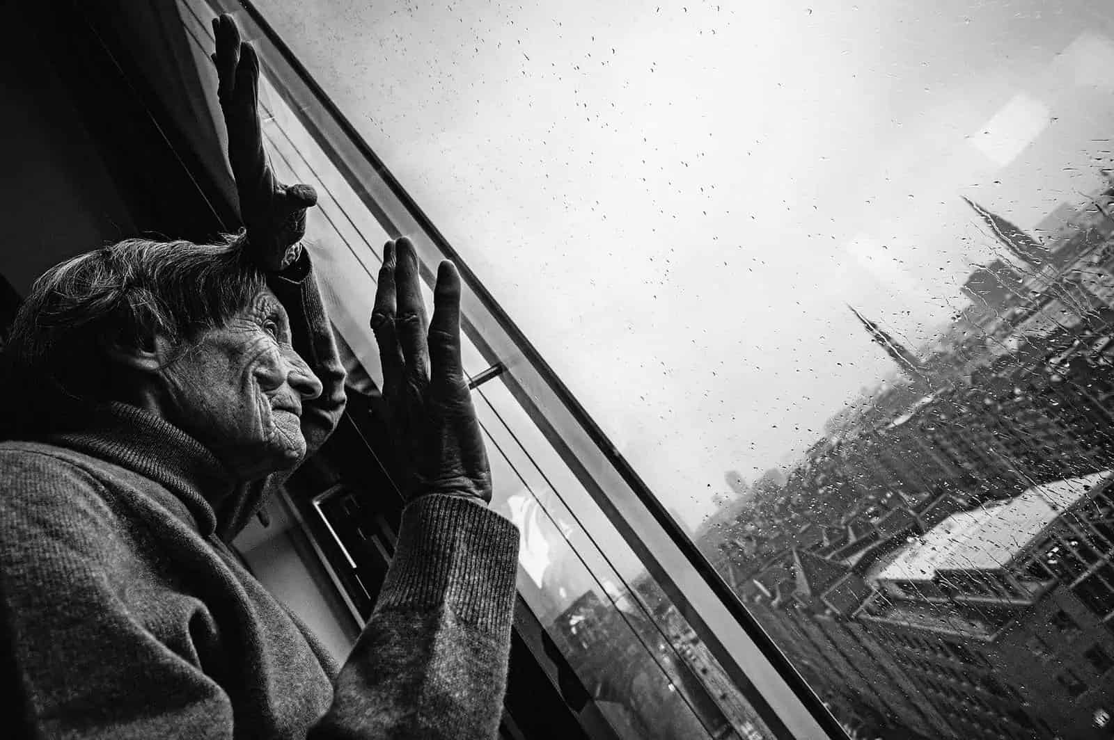 Mujer mayor mira por ventana lluviosa la metrópoli del Elba en libro fotográfico sobre Hamburgo.
