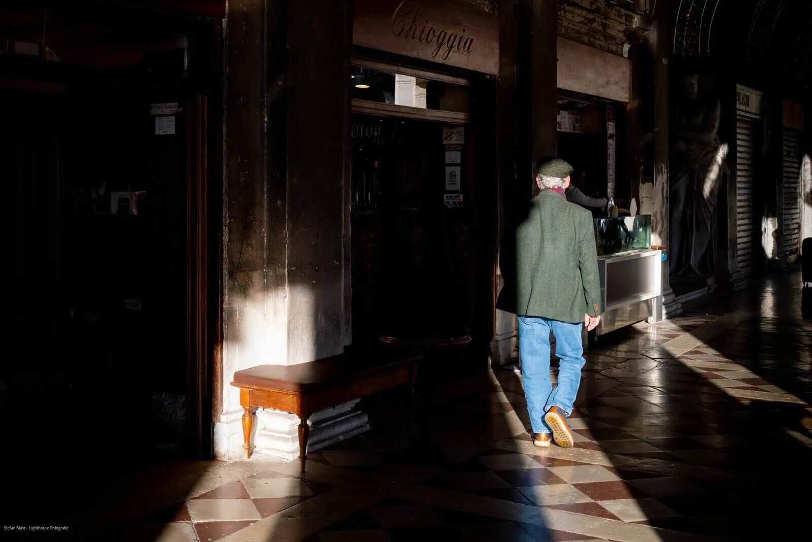 Hombre con chaqueta verde camina bajo luz solar en pasillo, fotografía como forma de omitir.