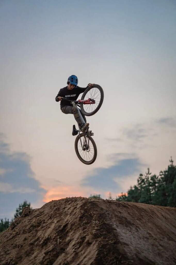 Ciclista de BMX realiza truco aéreo sobre montículo de tierra al atardecer.