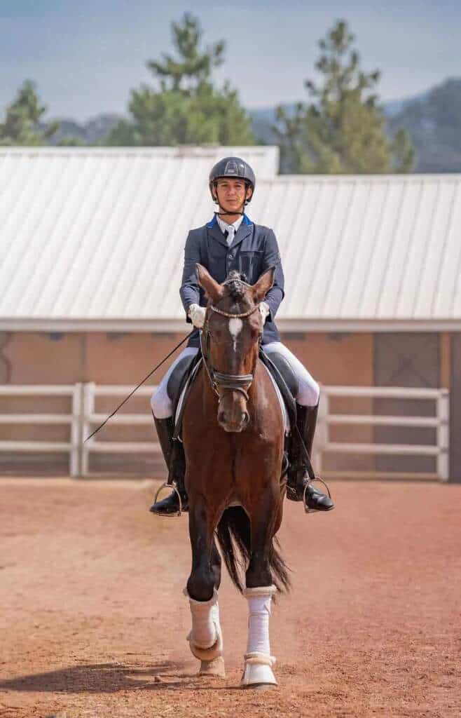 Joven jinete con casco y traje azul monta un caballo castaño en un día soleado.