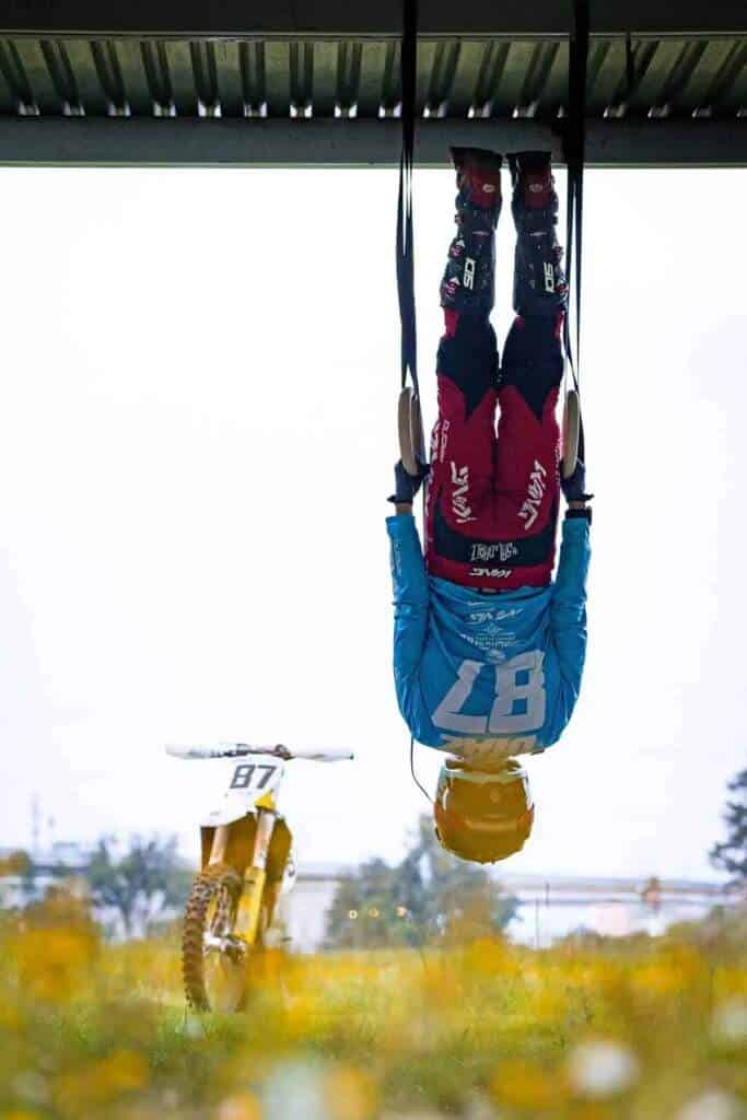 Ciclista de BMX colgado de anillas, con moto de fondo, arte y deporte combinados.