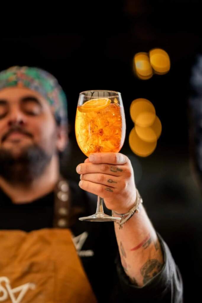 Fotógrafo de BMX sostiene un Aperol Spritz con rodaja de naranja y hielo.
