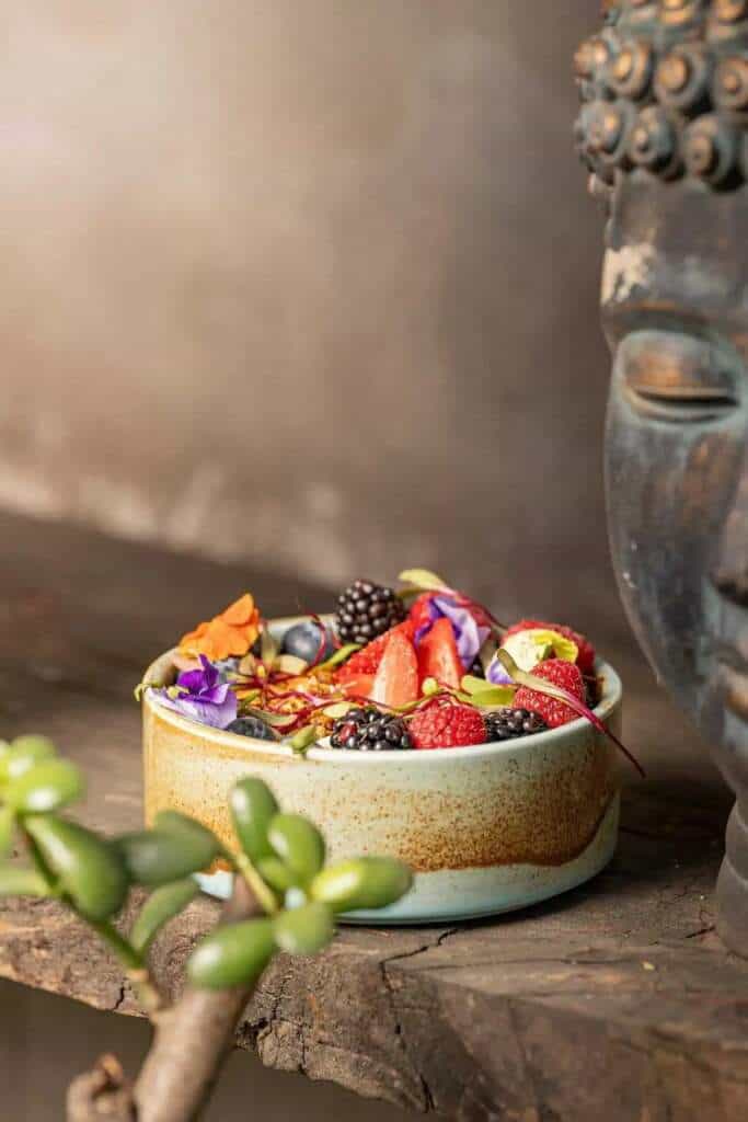 Tazón de frutas y flores junto a una estatua de Buda, arte y deporte combinados.