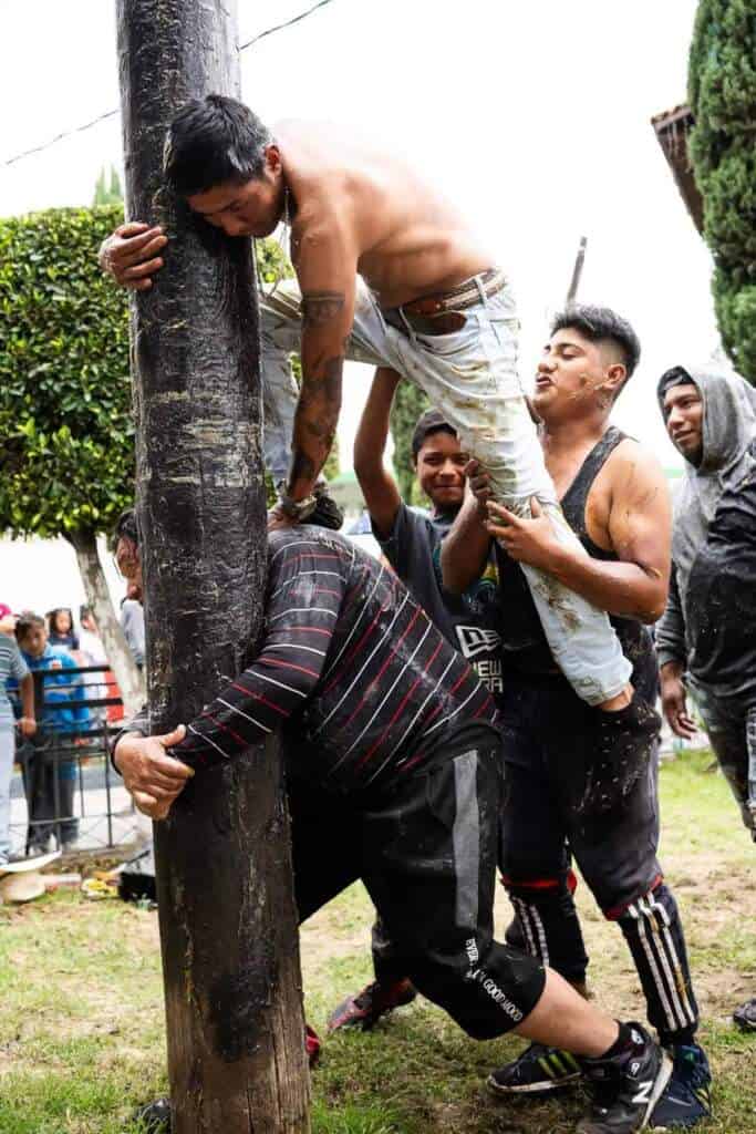 Hombres se ayudan a subir un poste resbaladizo en Tlaxcala durante el palo encebado.
