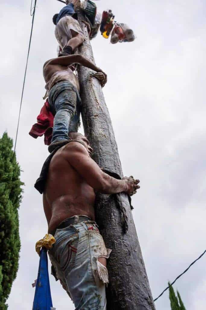 Hombres cubiertos de lodo escalan un palo encebado en Tlaxcala.