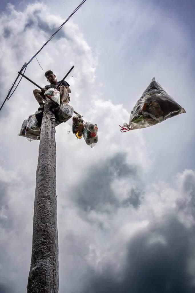 Joven en la cima de un palo encebado en Tlaxcala con bolsas de víveres.