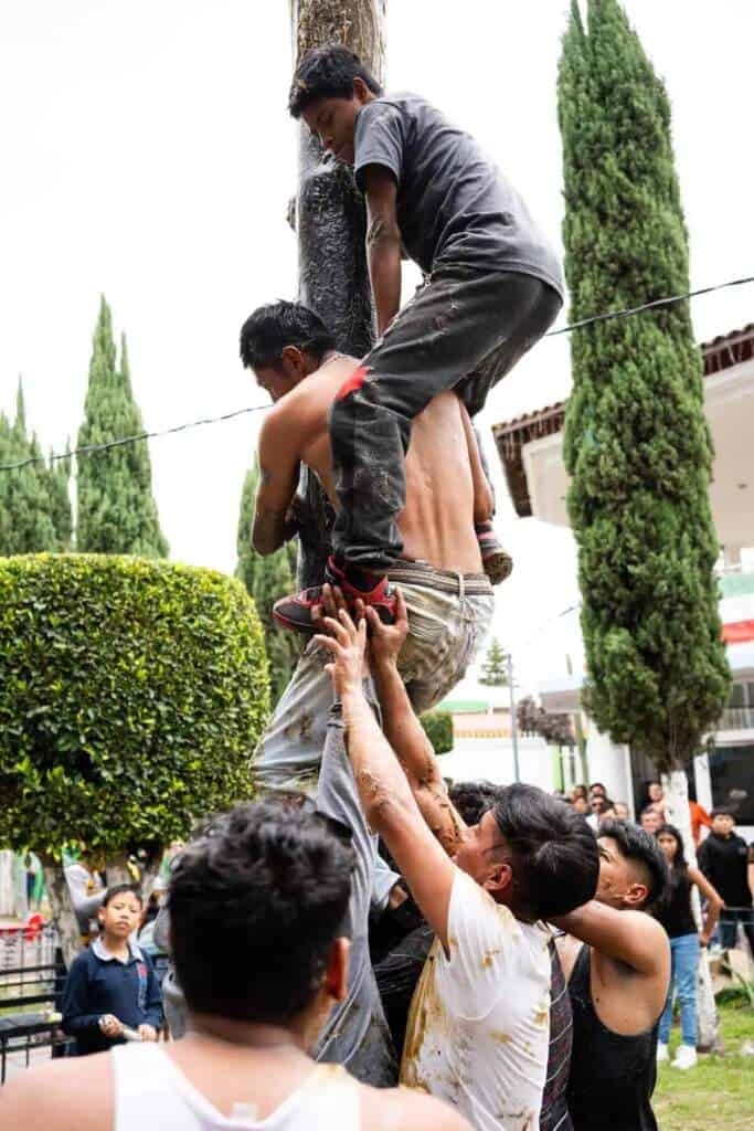 Jóvenes se ayudan para subir el palo encebado en Tlaxcala durante fiestas.