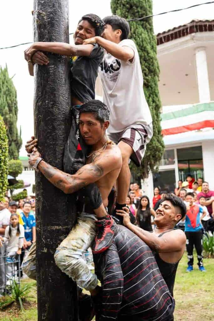 Hombres se esfuerzan por subir un palo encebado en Tlaxcala durante una fiesta.