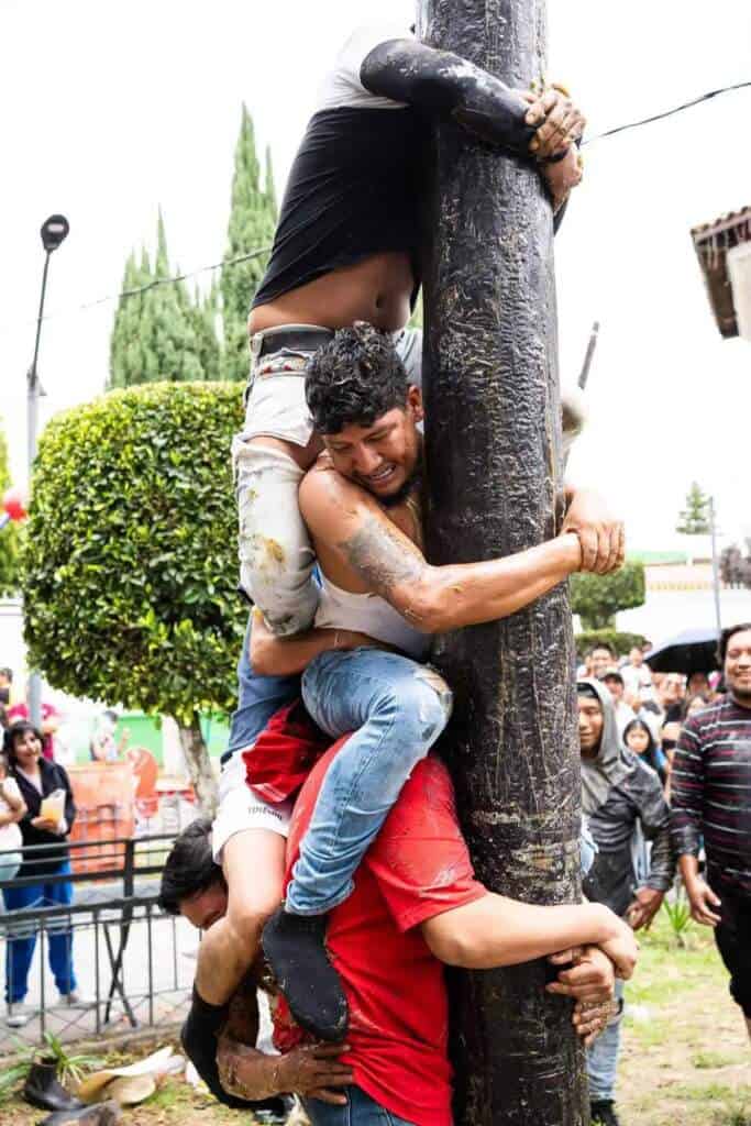 Hombres luchan por subir un palo encebado en Tlaxcala durante fiestas.