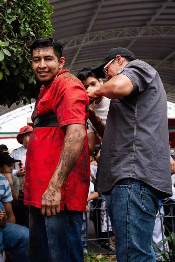 Hombre con camisa roja manchada de lodo en palo encebado en Tlaxcala